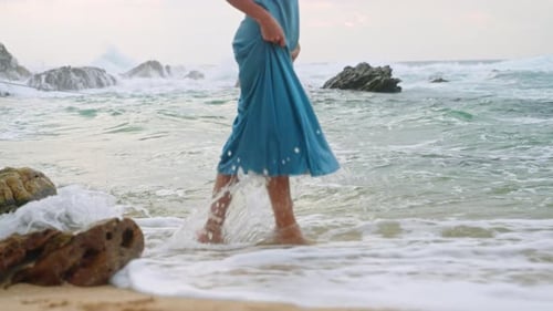 Elegant Woman in Blue Sun Dress Strolls Barefoot By Sea Serene Female Enjoys Peaceful Beach Walk at