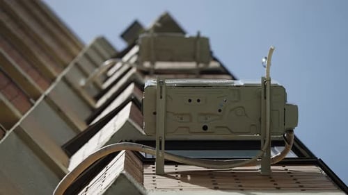 Perspectiva ascendente de gabinetes de equipamentos de telecomunicações montados ao longo da fachada de um edifício