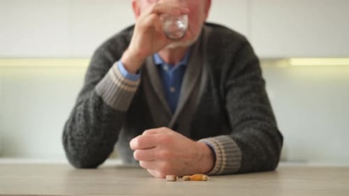 Senior Man Takes Pills with Water in Kitchen