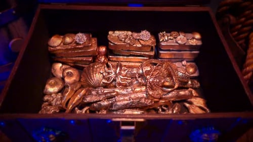 Zoomez sur un coffre au trésor rempli de lingots d'or, de diamants et d'autres objets de valeur.