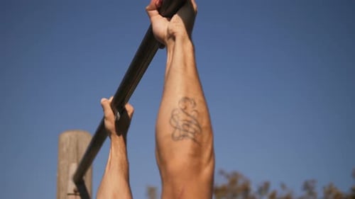 fit bleiben - junger Mann trainiert im Park und macht Klimmzüge an der Bar