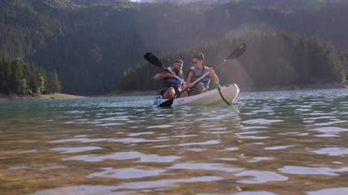 Enjoying scenic mountain landscape, two tourists paddling transparent lake waters during bright summ