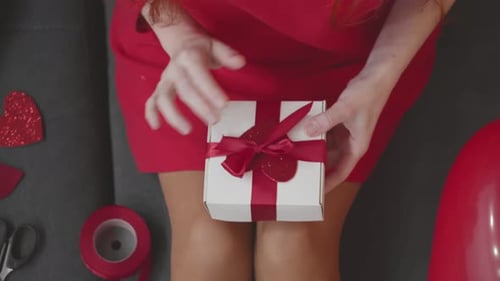 Woman Tying Red Ribbon On Gift For Loved One