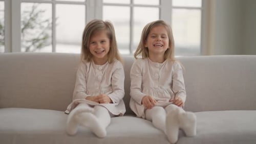 Two Happy Girls Laughing on Sofa Indoors
