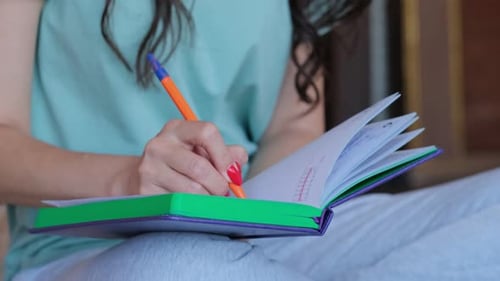 Woman Writing in Notebook with Orange Pen Indoors