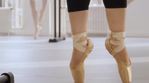 Ballet dancers practising their pointe techniques with a black ballet barre in a dance studio. Close
