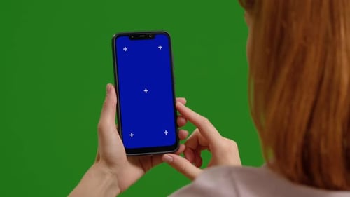 Woman hands taps and scrolls green blue mock up chromakey phone on green screen background.