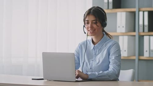 Woman at Desk with Headset Typing on Laptop