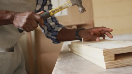 Mid section of african american male carpenter hammering nails into the wood at a carpentry shop