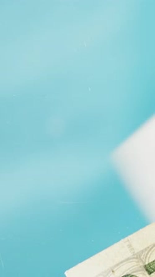 Vertical video. Close-up, twenty-dollar bills falling onto a glass table. View from below.