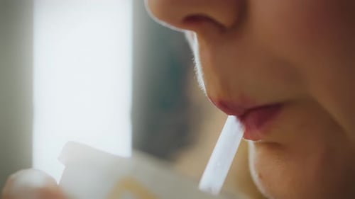 In a fast food street eatery, a beautiful girl enjoys a chilled soda cola with ice using a straw. A