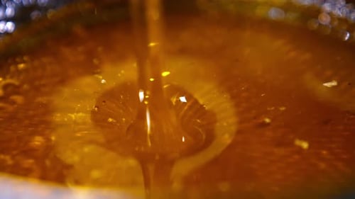 Flow of yellow fresh honey falling into the bowl.