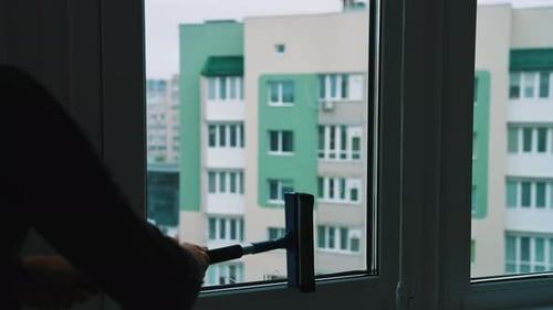 Mann putzt das Fenster und drückt Wasser mit einer Bürste aus. Männlicher Arbeiter wäscht Glas in der Wohnung.