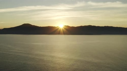 Beautiful aerial drone view sunset over the ocean and mountains on the horizon.