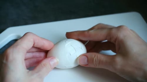 Hands Peeling a Freshly Boiled Egg on Cutting Board