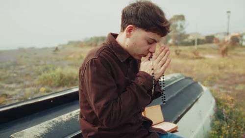 Young Adult Praying with Rosary in Nature