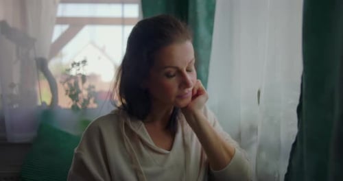 Woman in Hoodie Contemplative, Sitting by Window