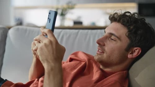 Smiling Man Relaxing on Couch Using Smartphone