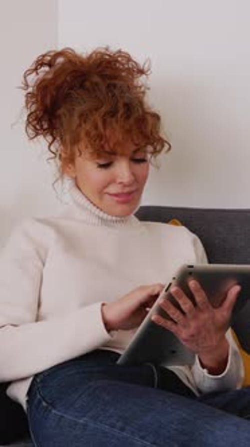 Woman Sitting on Sofa Using Tablet Indoors