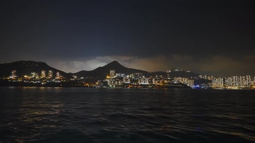 Shot from a boat traveling to the left of an urbanized island in the middle of the night.
