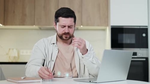 Overloaded Man Taking Off Glasses and Rubbing Eyes While Working By Laptop