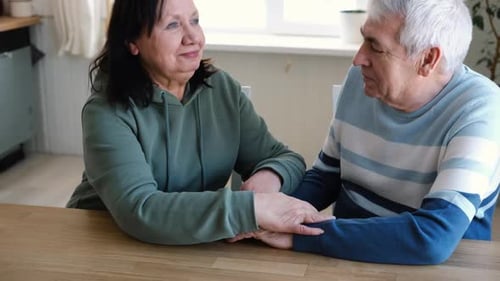 Senior Couple Holding Hands and Talking in Kitchen