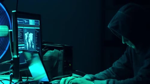 Hooded Man Working on Multiple Computer Screens
