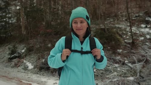 Portrait of charming smiling female with backpack hiking in winter forest