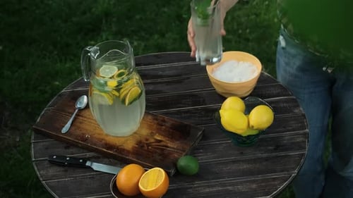 Woman Puts Glass of Refreshing Homemade Lemonade on Wooden Garden Table