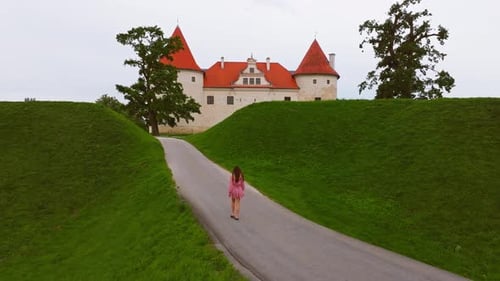 Woman Walks Toward Bauska Castle on Cloudy Day – Scenic Establishing Shot