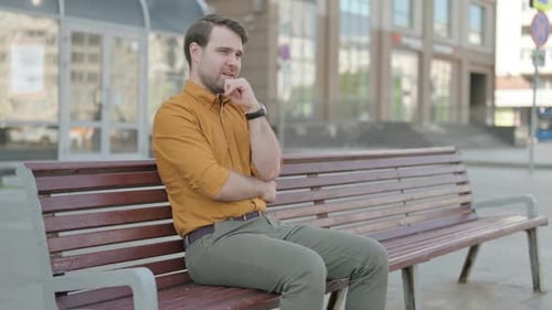 Pensive Young Man Thinking while Sitting Outdoor on Bench