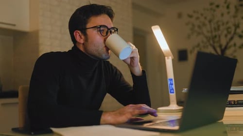 Young Man Working at Night with Coffee and Laptop in Cozy Home Office