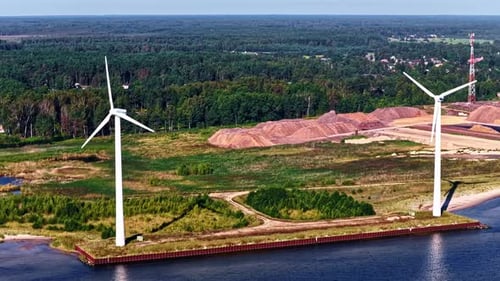 Green energy wind turbines at coastal industrial site from drone view