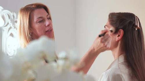 Female Makeup Artist Applying Blusher with Brush on Woman's Face in Studio