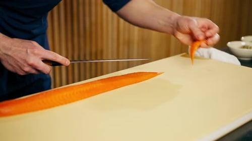 Close Up in a Japanese Restaurant Chef in a Blue Uniform Cuts Fish for Sushi Into Slices on a Yellow