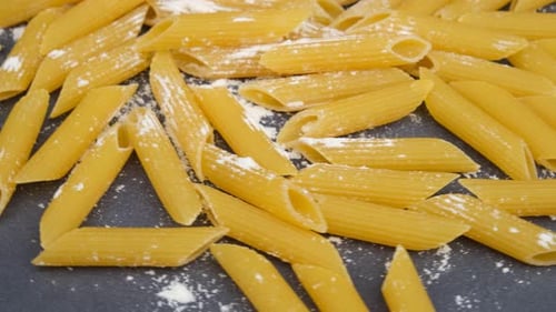 Uncooked Penne Pasta Scattered on Gray Background