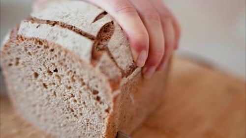 Person Slicing Fresh Bread Loaf with Knife