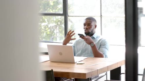 Using smartphone and laptop, man working at office desk, multitasking