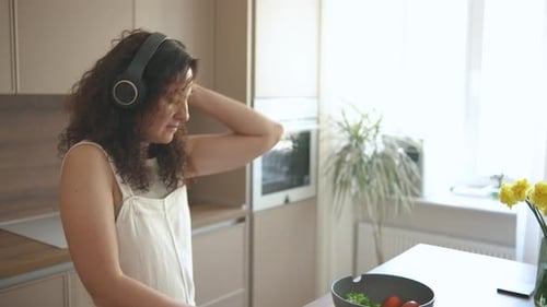 Woman with Headphones Cuts Cucumber, Dances in Kitchen