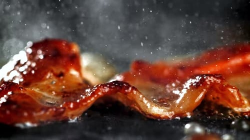 Sizzling Bacon Cooking on a Black Surface