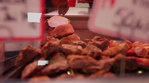 Man filling the fridge with smoked loin pieces in a shop window for sale.