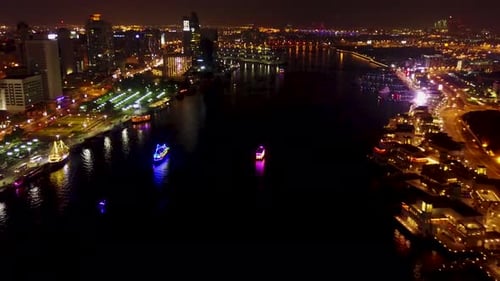 A Vibrant Night Scene Shows a Breathtaking Riverside Cityscape with Colorful Boats on the Water