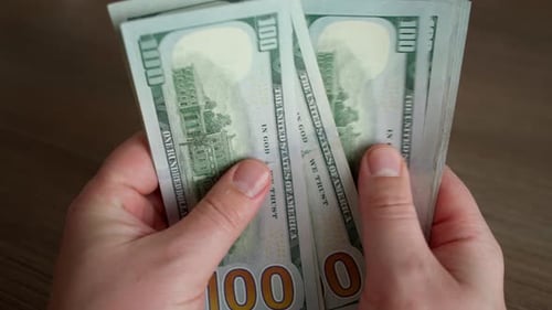 Close-up of a man's hands counting a stack of hundred dollar bills.