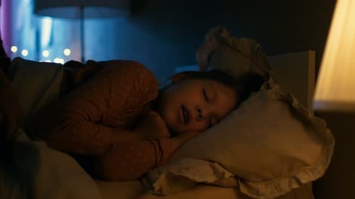Sweet Little Girl Sleeps in Her Bed at Night, Her Mother Tucks Her Blanket in.