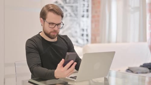 Adult Man Uses Phone at Laptop