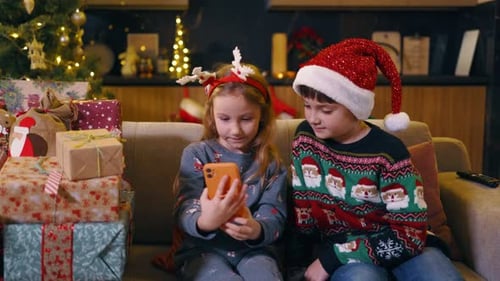 Children Watching Phone by Christmas Tree and Presents