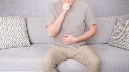 Man Sitting Coughing and Rubbing Stomach at Home