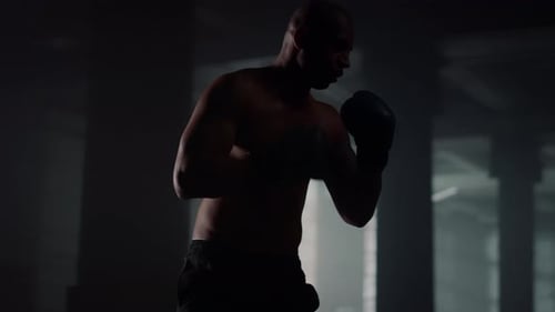 Man Boxing with Punching Bag in Dark Gym
