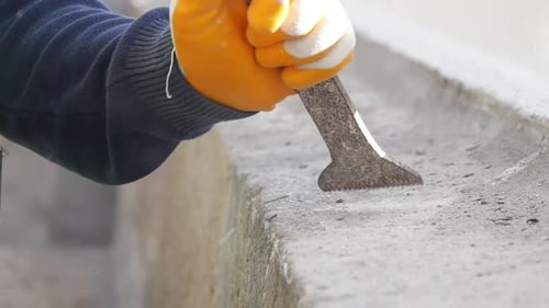 Gloved Hands Scraping Concrete Surface with Tool