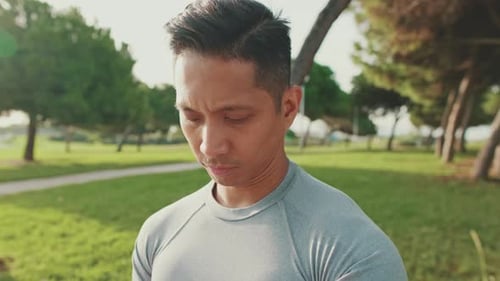Close-up of a young man sitting on a bench and looking down at smart watch, mobile phone